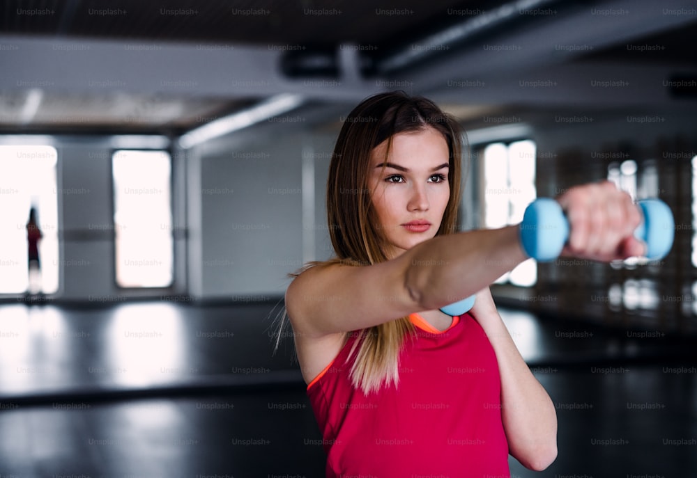 A portrait of a beautiful young girl or woman doing exercise with a dumbbells in a gym.