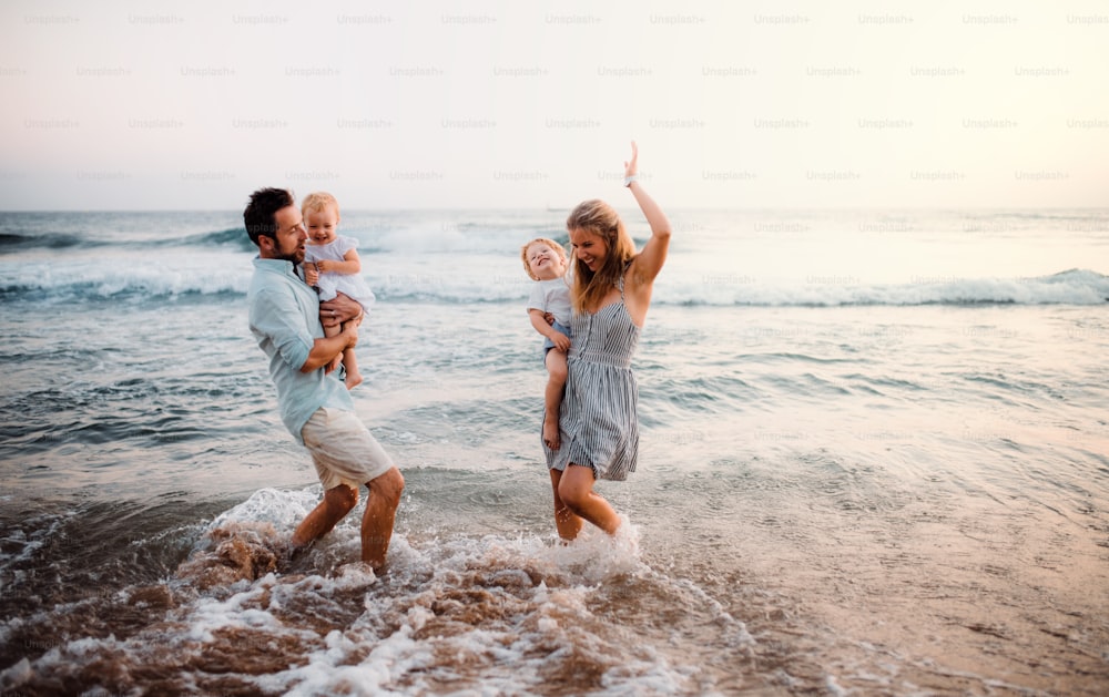 Una giovane famiglia con due bambini piccoli in piedi sulla spiaggia durante le vacanze estive, divertendosi.