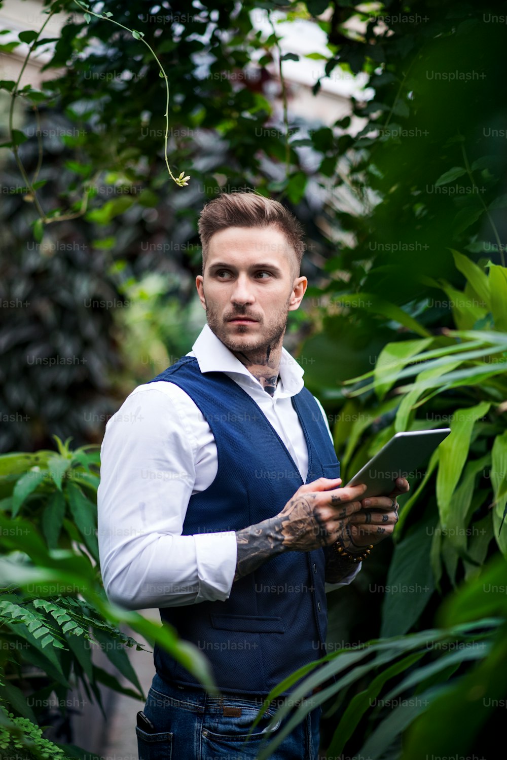 植物園に立つタブレットを持つ青年。グリーンビジネスのコンセプト。