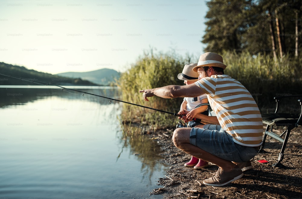 Un padre maturo con un figlio piccolo all'aperto che pesca in riva a un fiume o a un lago.