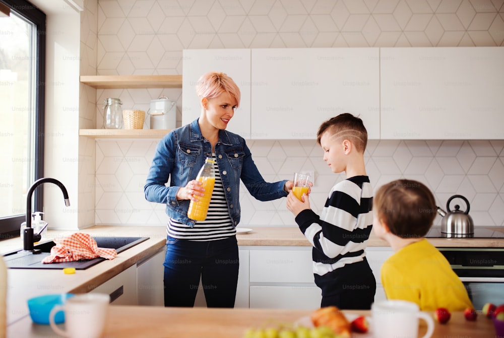 Una giovane donna con due bambini felici che beve succo d'arancia in una cucina.
