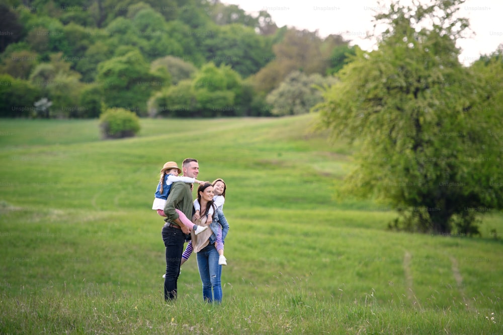 Famiglia felice con due figlie piccole in piedi all'aperto nella natura primaverile, tiro lungo.