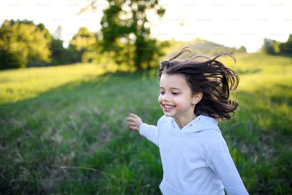 Portrait of cheerful small girl running outdoors in spring nature, laughing.