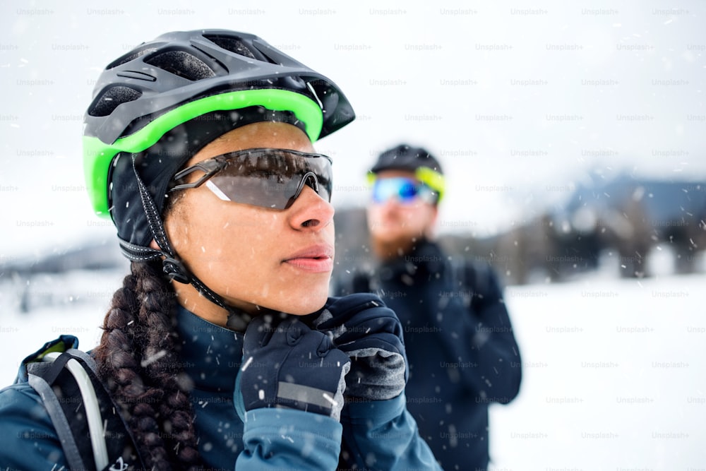 Two mountain bikers standing outdoors in winter, putting on helmet.
