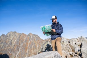 Uomo maturo che fa escursioni in montagna in estate, usando la mappa. Copia spazio.
