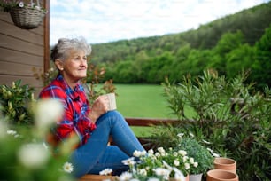 Portrait d’une femme âgée avec un café assis sur la terrasse en été, se reposant.