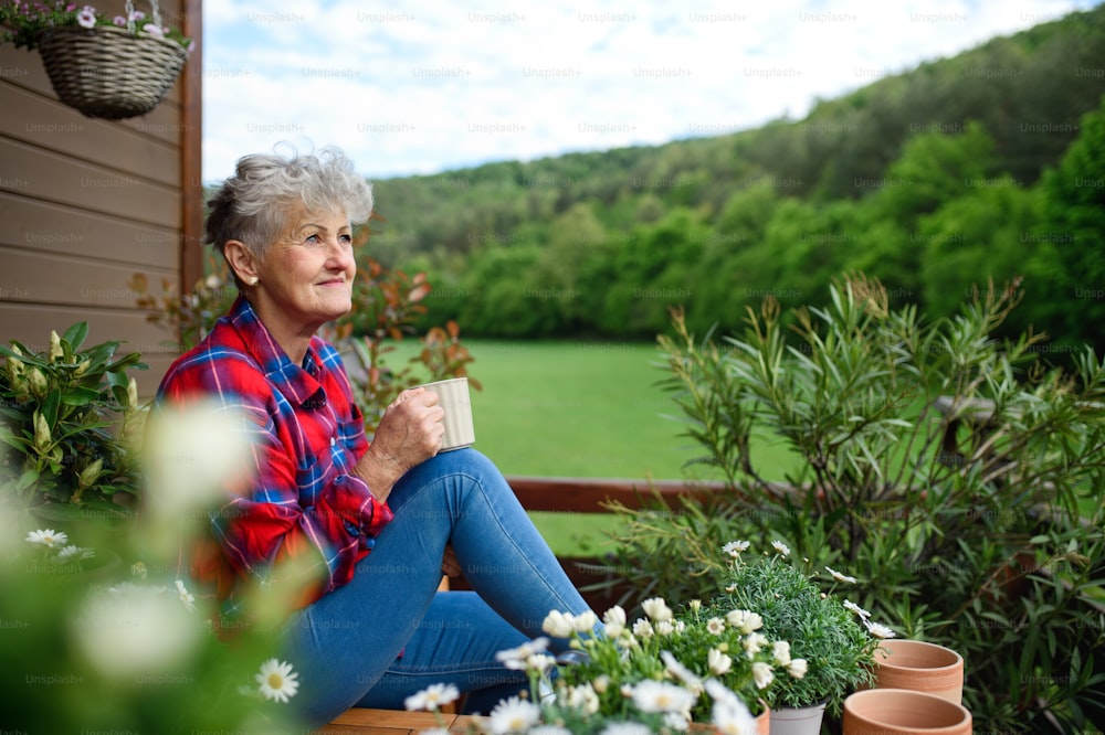 Retrato da mulher idosa com café sentado no terraço no verão, descansando.