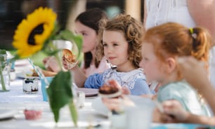 Niñas pequeñas felices sentadas y comiendo en la mesa en la fiesta del jardín de verano, concepto de celebración de cumpleaños.