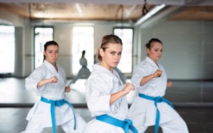 Eine Gruppe junger Frauen übt Karate drinnen im Fitnessstudio.