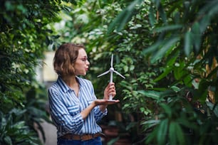 Mujer joven de pie en el jardín botánico, sosteniendo el modelo del molino de viento. Espacio de copia.