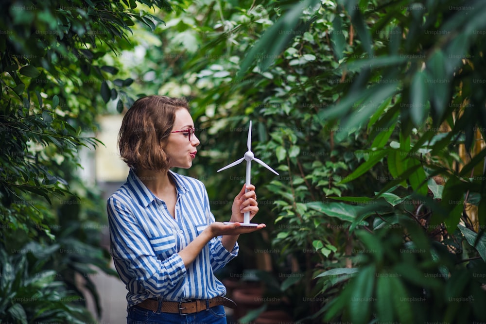 Young woman standing in botanical garden, holding windmill model. Copy space.