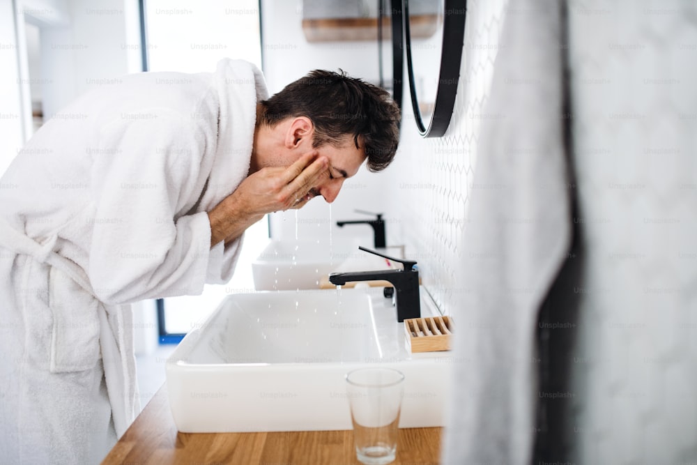 Jeune homme se lavant le visage dans la salle de bain le matin, une routine quotidienne.