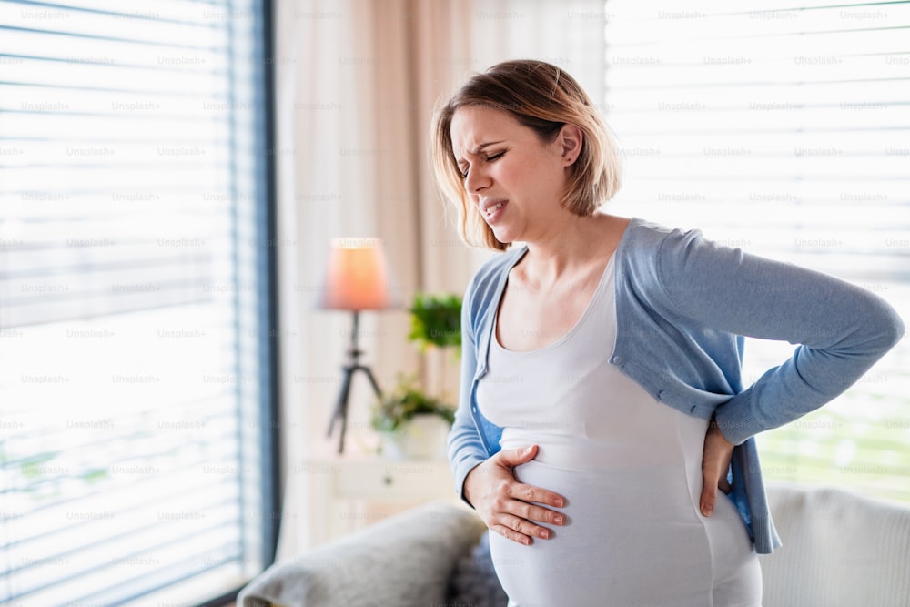 Taillenporträt einer schwangeren Frau mit Schmerzen in Innenräumen zu Hause.
