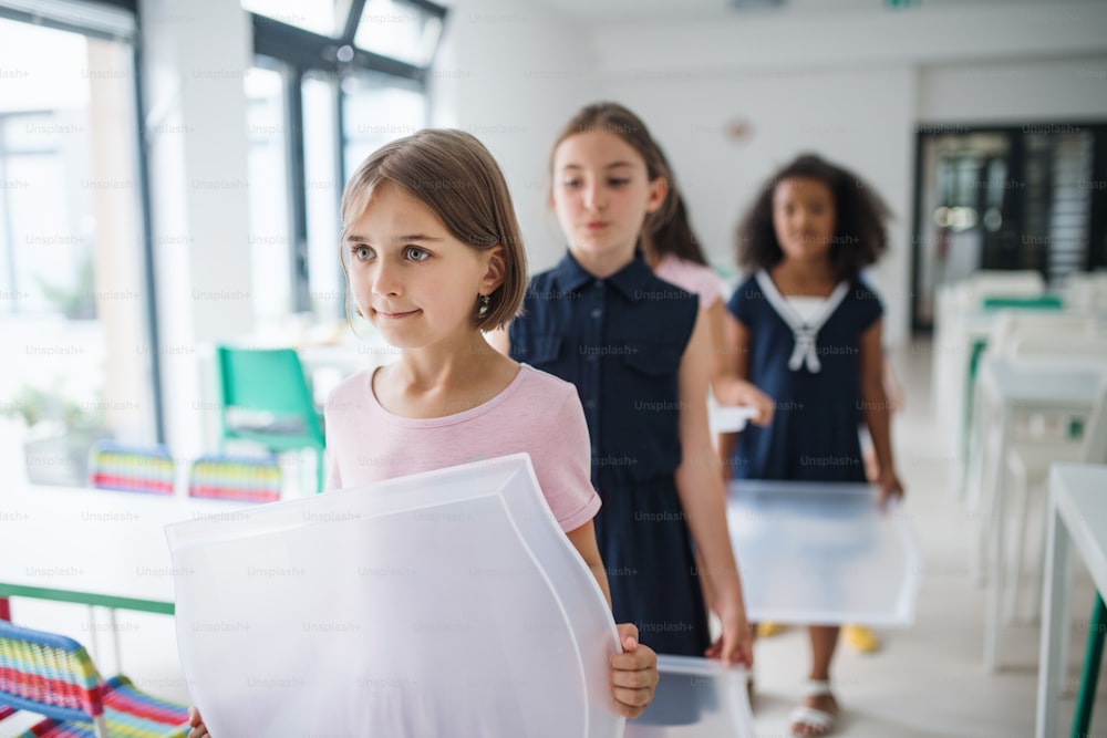 A group of cheerful small school kids with plastic trays in canteen, walking.