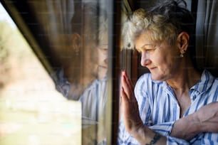 Traurige ältere Frau, die drinnen am Fenster zu Hause steht, Coronavirus und Quarantänekonzept.