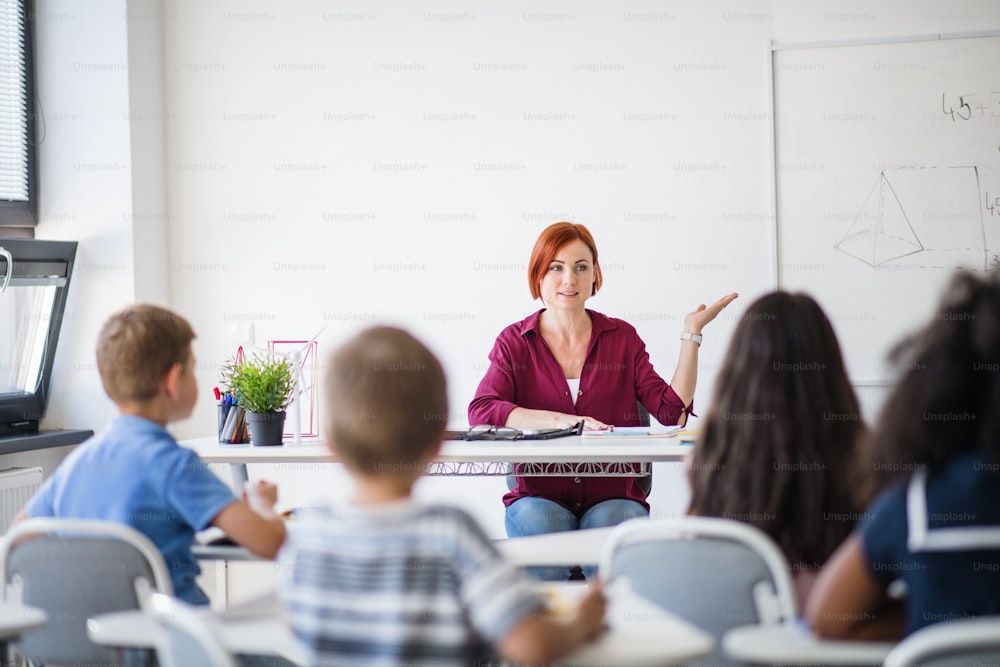 Vue arrière d’écoliers assis au bureau de la salle de classe pendant la leçon, écoutant l’enseignant.