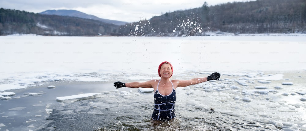 冬の水の中で屋外の水着を着たアクティブなシニア女性の正面図、風邪療法のコンセプト。