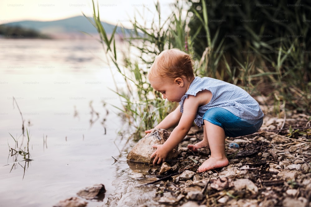 Una niña pequeña jugando al aire libre junto al río en verano. Espacio de copia.