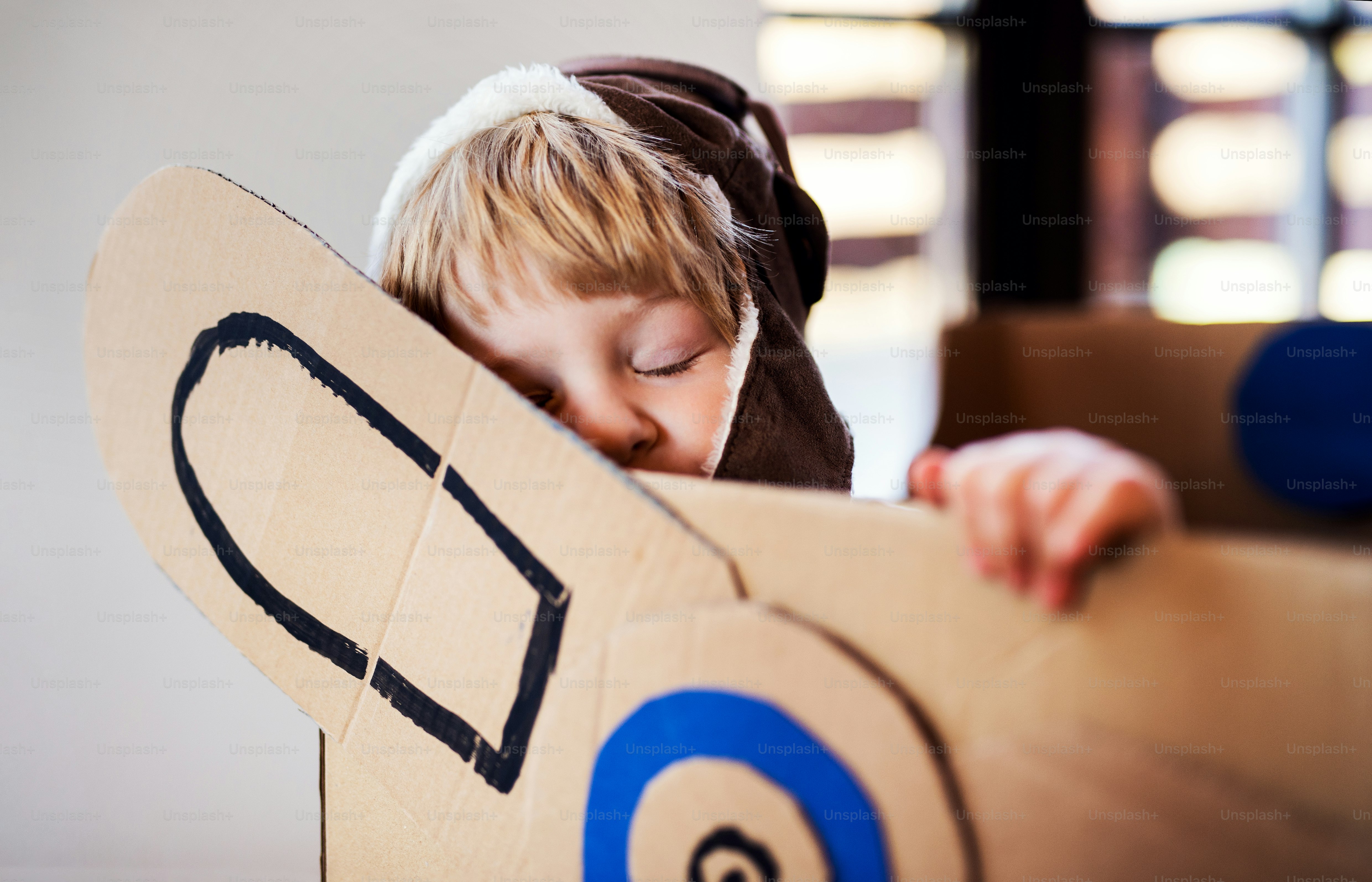 A happy toddler boy with carton plane playing indoors at home, flying concept.