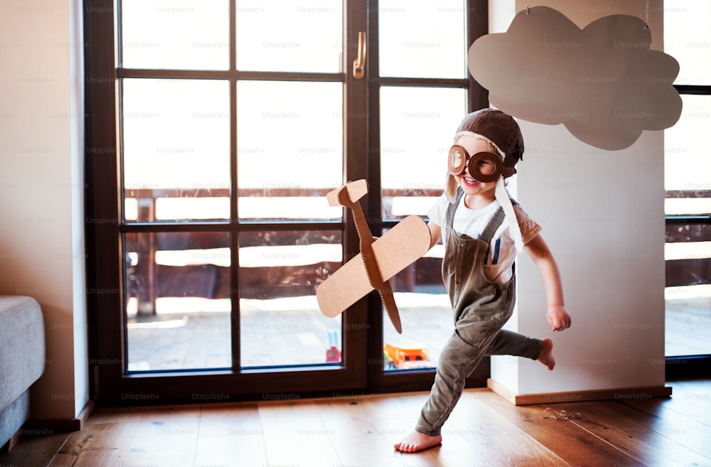 A toddler boy with carton plane and clouds playing indoors at home, flying concept.