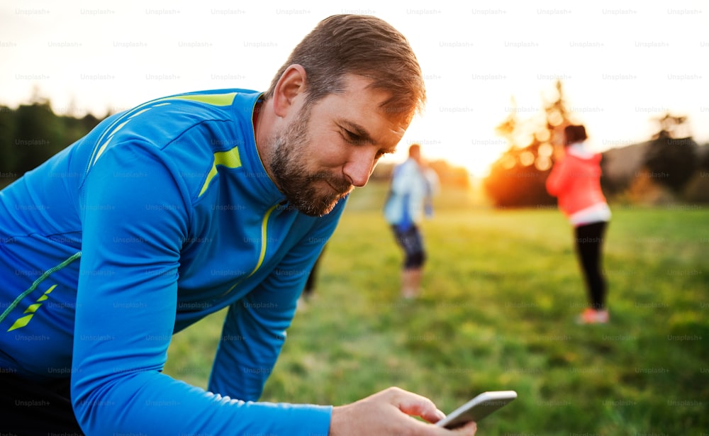 自然界の人々のグループと運動をした後にスマートフォンを使用する男性。