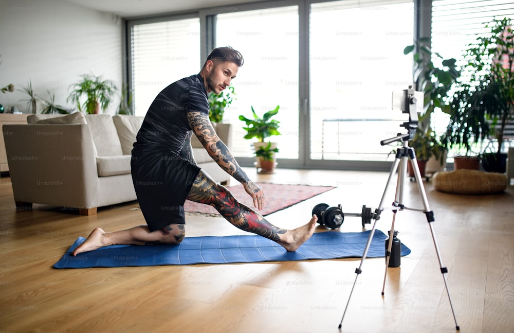Young man trainer doing online workout exercise indoors at home, using camera.
