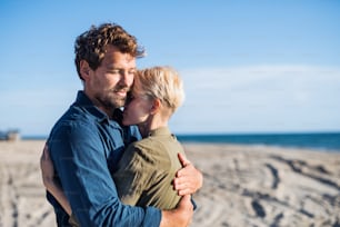 Una joven pareja de pie al aire libre en la playa, abrazándose. Espacio de copia.