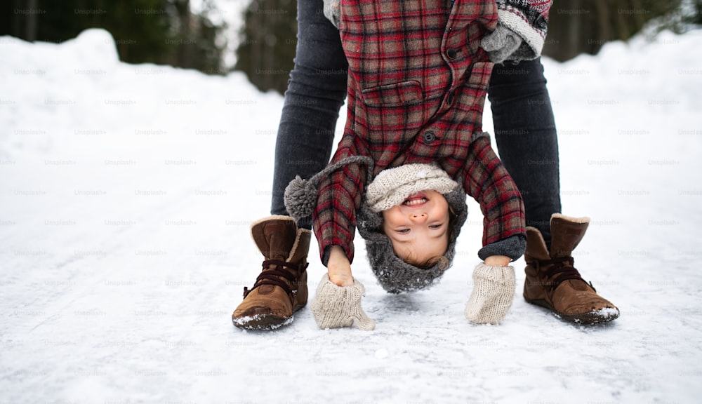 Midsection of unrecognizable mother holding small daughter upside down in winter nature.