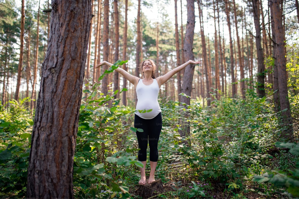 Front view portrait of happy barefoot pregnant woman outdoors in nature, doing exercise.