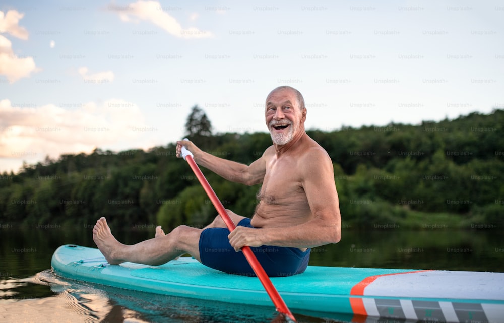 Vista frontale dell'uomo anziano paddleboarding sul lago in estate. Copia spazio.
