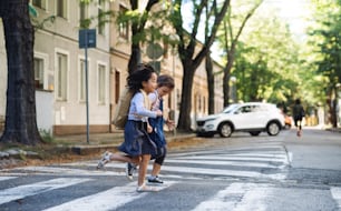 Cheerful small girls crossing street outdoors in town, coronavirus concept.