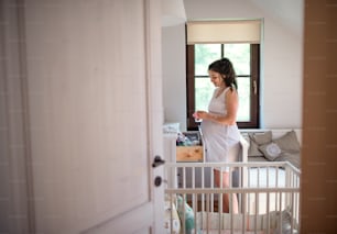 Pregnant woman indoors in bedroom at home, putting clothes in the drawer.