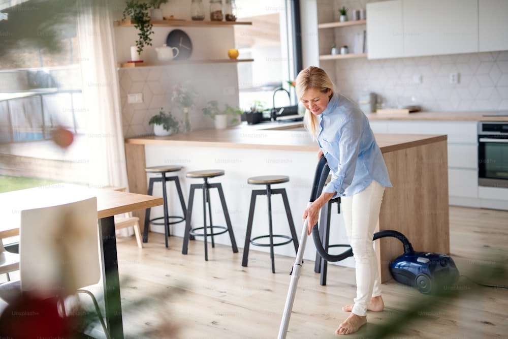 Retrato de una mujer mayor feliz con una aspiradora en el interior de la casa, aspirando.