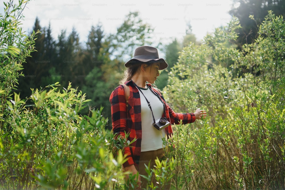 Vue de face d’une jeune femme avec un appareil photo lors d’une promenade en forêt dans la nature estivale.