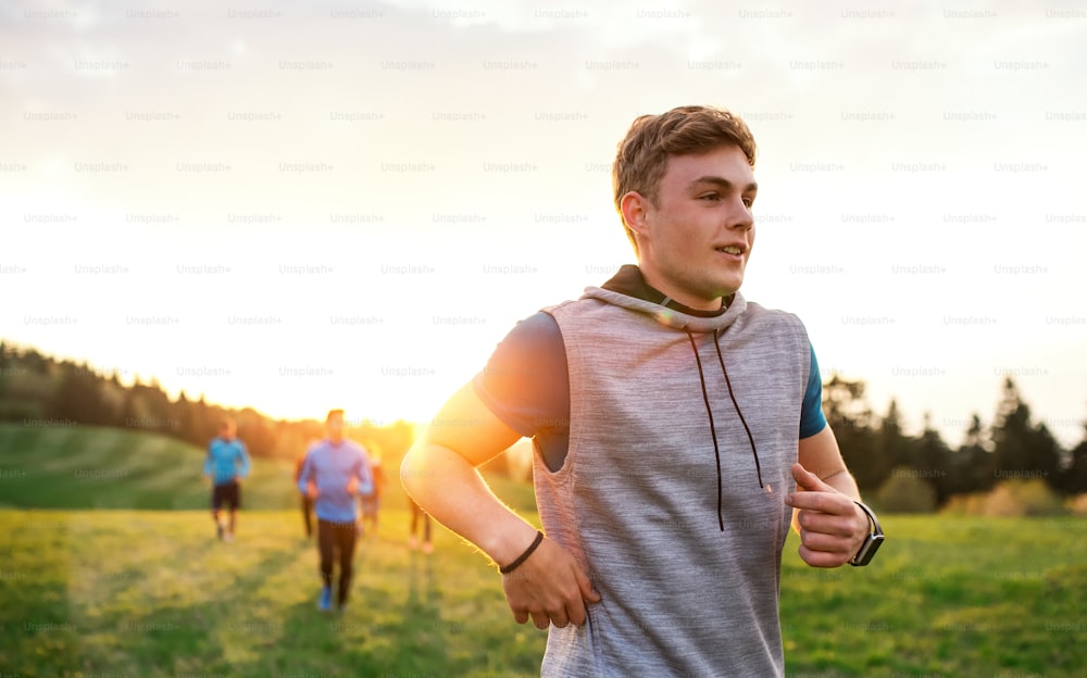 Um retrato de um jovem com grande grupo de pessoas fazendo exercícios na natureza, correndo.