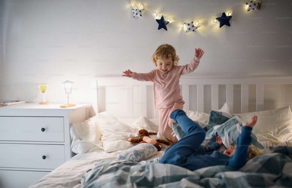 笑う2人の小さな子供が、自宅の室内のベッドに飛び乗って楽しんでいます。