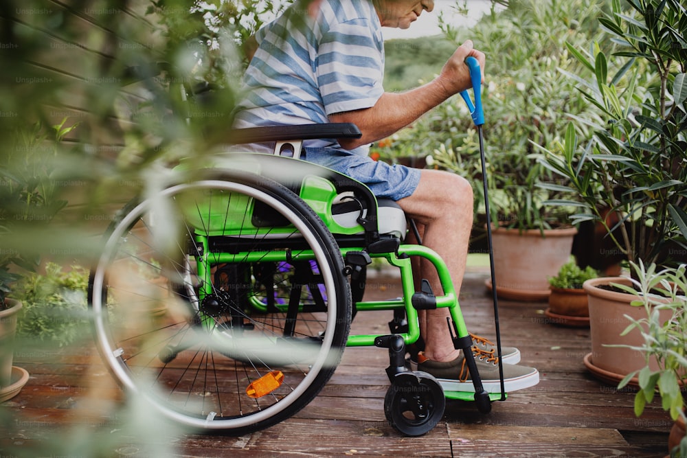 Un uomo anziano irriconoscibile in sedia a rotelle che fa esercizio sulla terrazza.