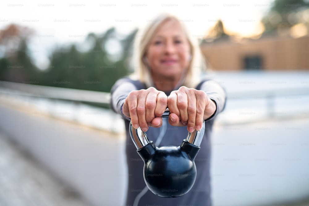 A senior woman with kettlebell outdoors doing exercise on terrace.