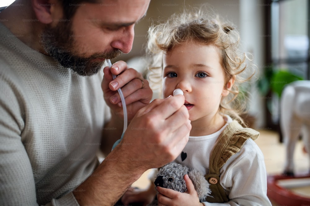 Reifer Vater mit kleiner kranker Kleinkindtochter drinnen zu Hause, mit Nasensauger.