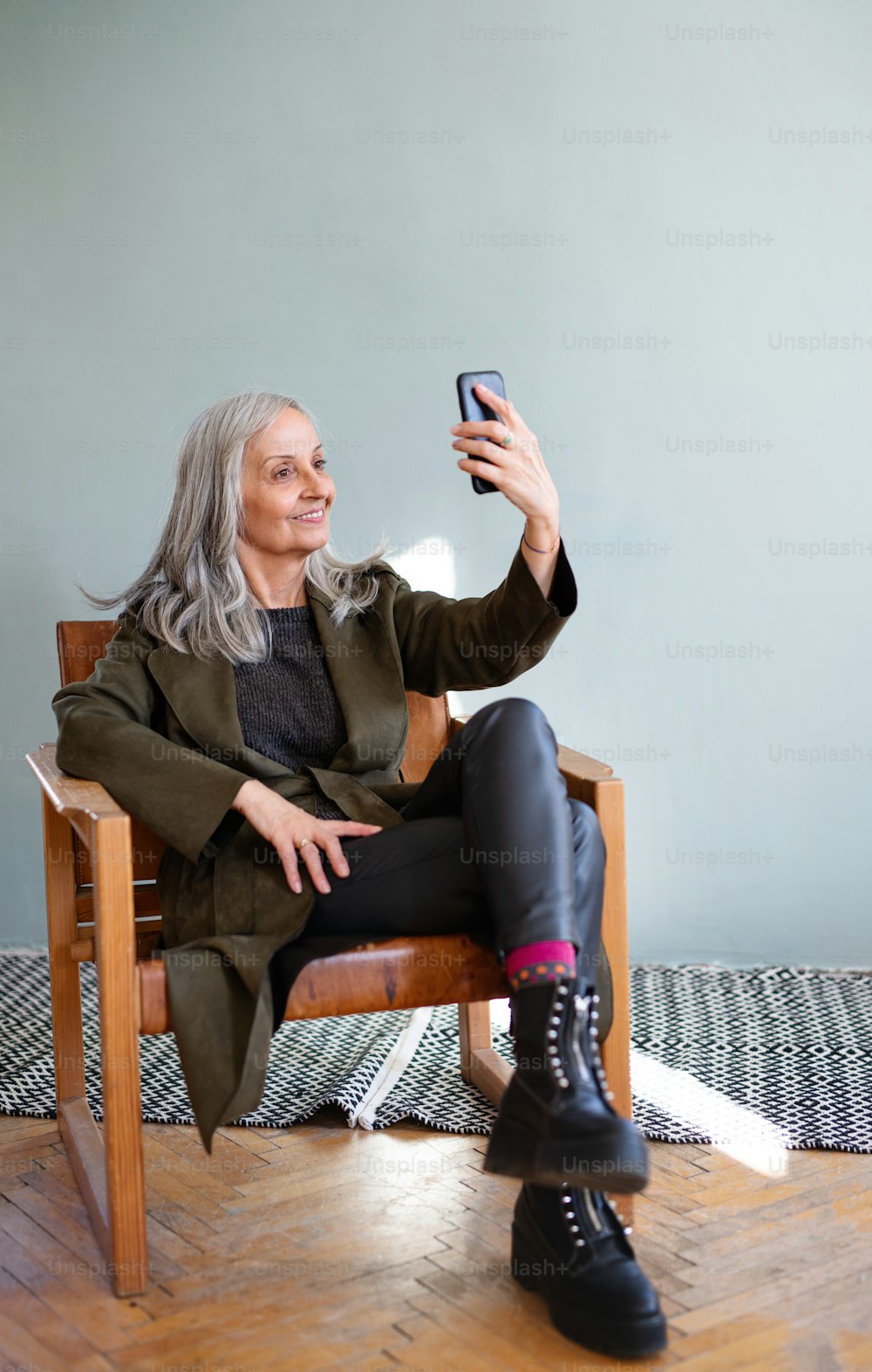 Portrait of senior woman with sitting indoors on chair, taking selfie with smartphone.