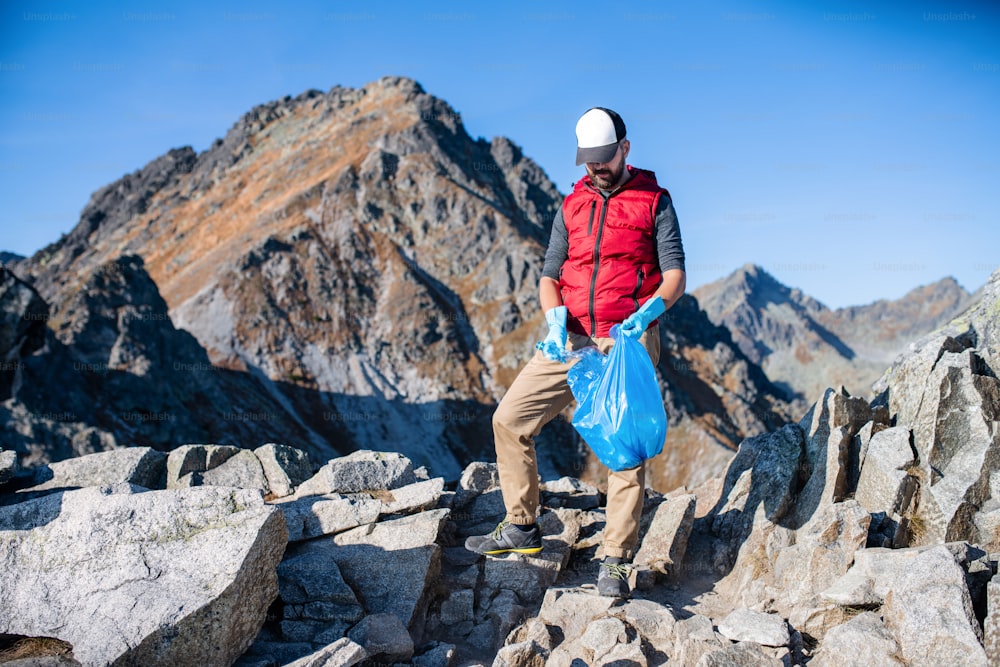 Escursionista uomo maturo che raccoglie rifiuti in natura in montagna, concetto di plogging.