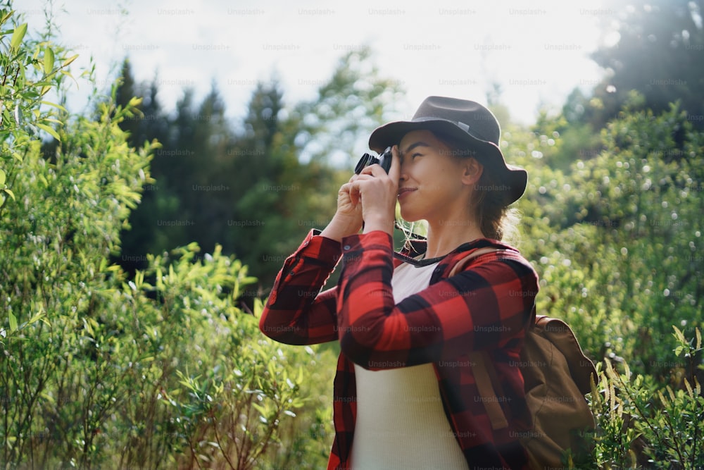 Vista laterale di giovane donna con un cane su una passeggiata all'aperto nella natura estiva, scattando fotografie.