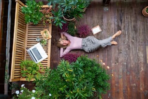 Una vista superior de una mujer mayor con una computadora portátil acostada al aire libre en la terraza, descansando.
