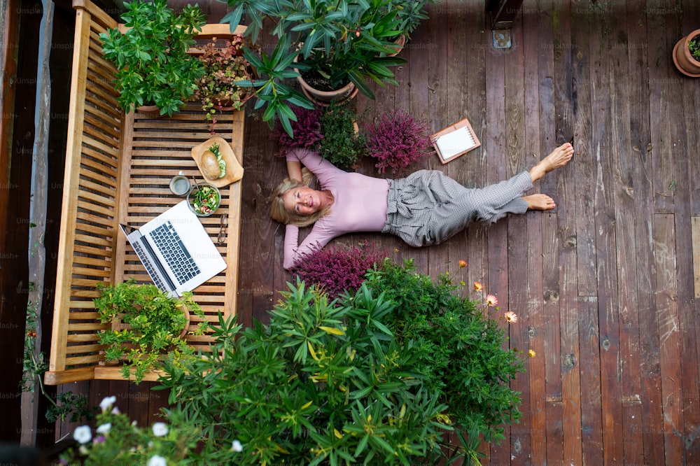 Uma vista superior da mulher idosa com laptop deitado ao ar livre no terraço, descansando.