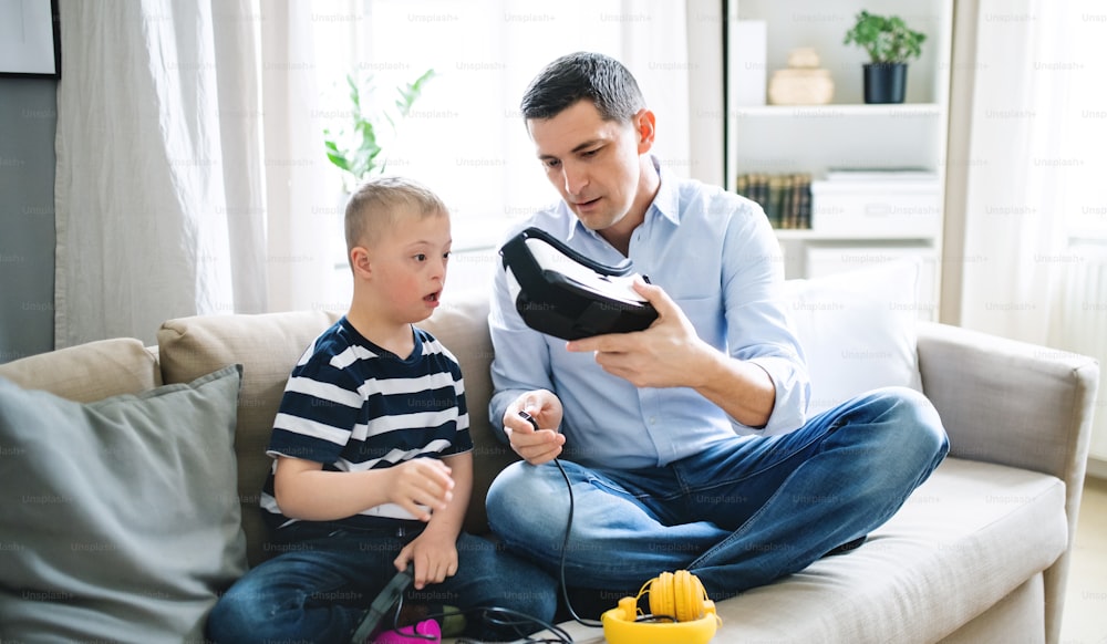 A father with happy down syndrome son indoors at home, using vr goggles.