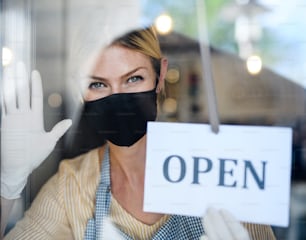 Coffee shop woman owner with face mask, open after lockdown quarantine. Shot through glass.