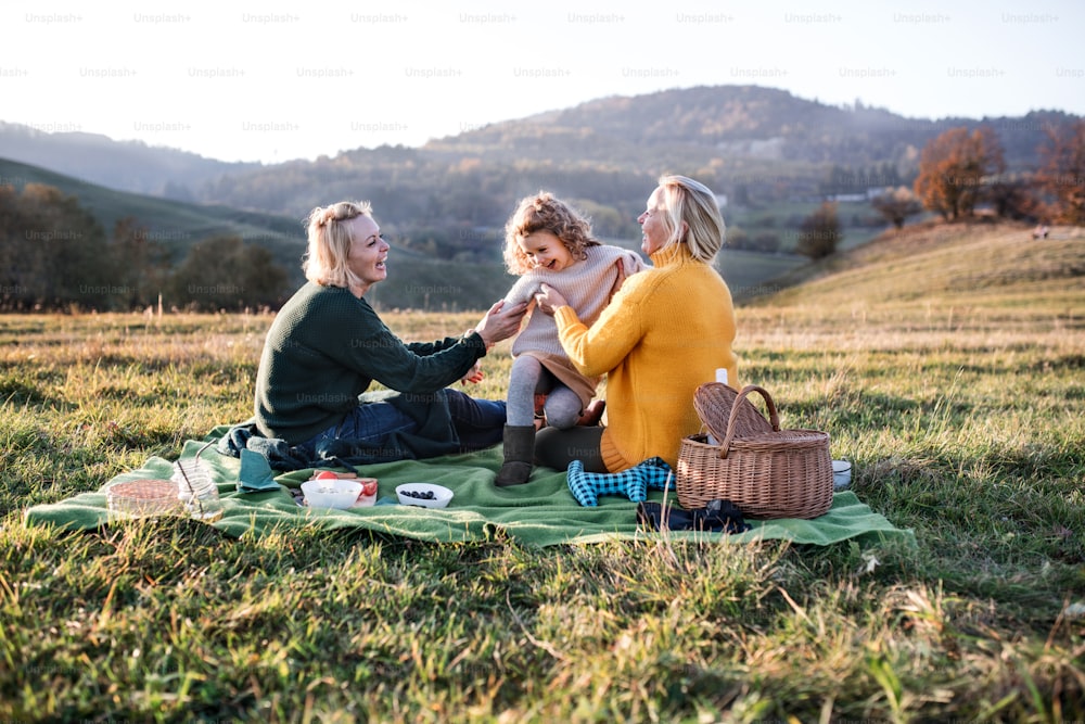 夕暮れ時に自然の中でピクニックをしている母と祖母を持つ幸せな小さな女の子。