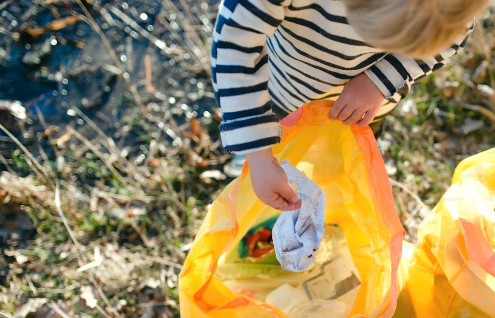 Midsection of unrecognizable small child collecting rubbish outdoors in nature, plogging concept.