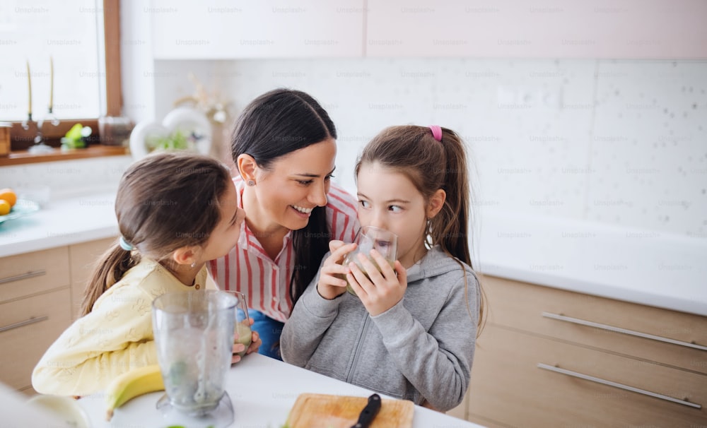 Mother with girls indoors at home, preparing healthy fruit smoothie drink.