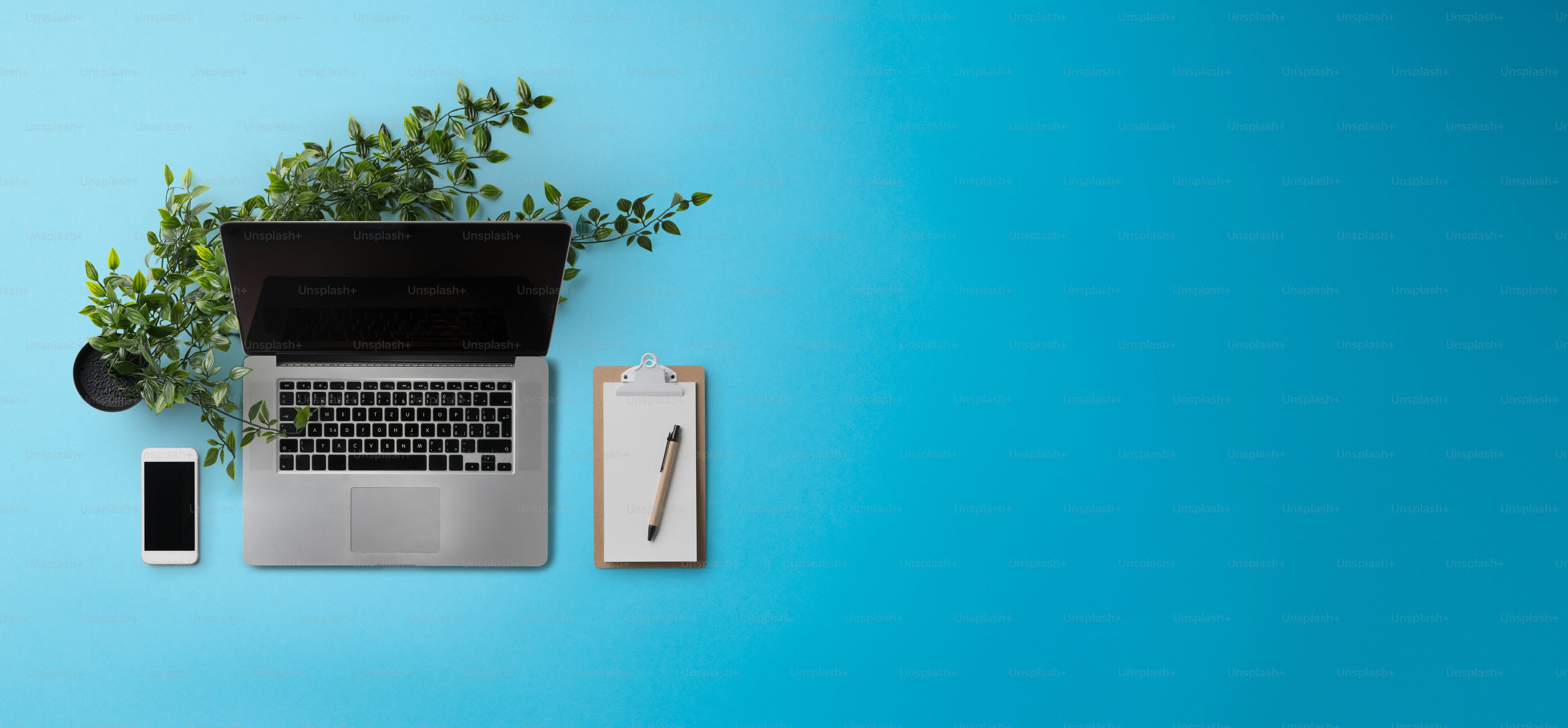 Flat lay top view office desk working space with laptop and smartphone on blue background. Copy space.